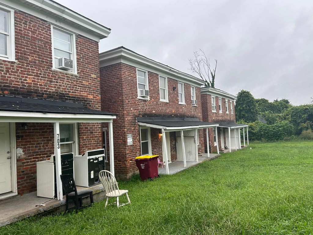 the front of a brick building with a lawn and a rocking chair