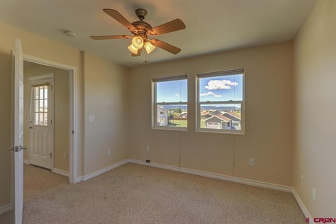 A room with a ceiling fan and two windows.