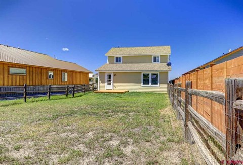 A wooden fence surrounds a grassy yard with a two-story house in the background.
