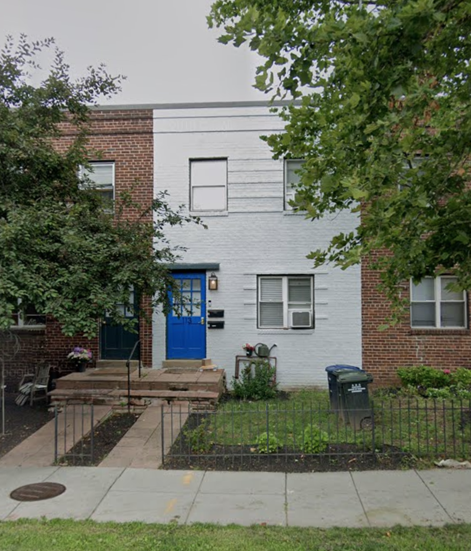 A white and red brick house with a blue door and a black trash can.