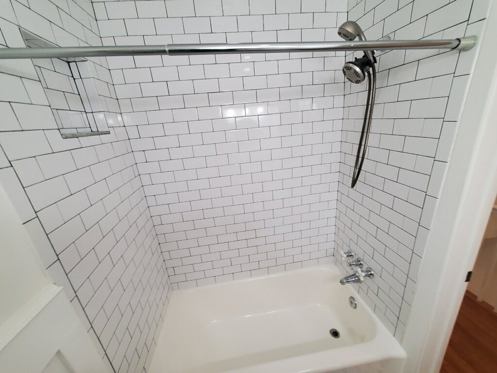 A white tiled shower with a white tub and a silver shower head.