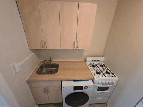 A small kitchen with a stove, sink, and washer.