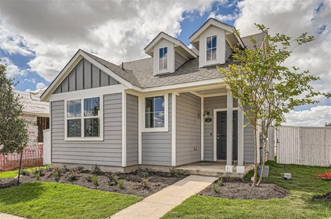 the front of a gray house with a yard and a tree