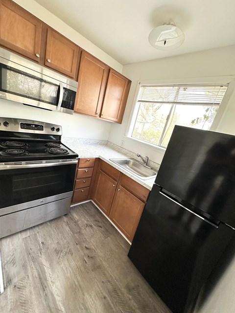 A black refrigerator is in a kitchen with wooden cabinets and a stove.