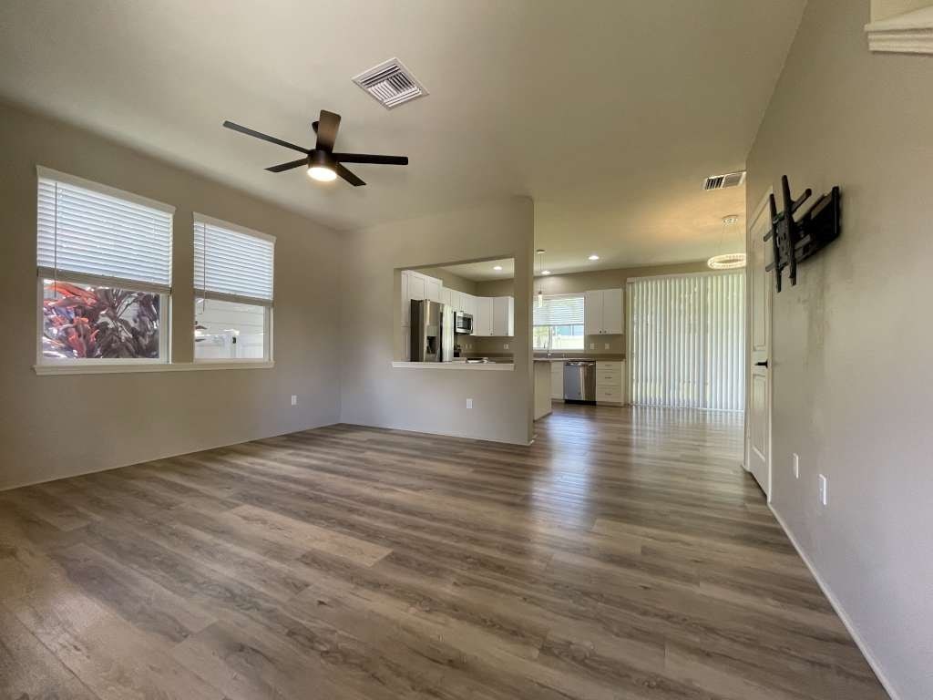 an empty living room with a ceiling fan and a kitchen
