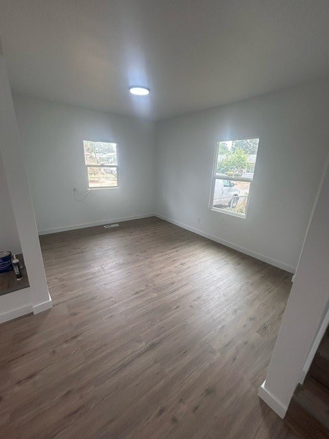 A room with wooden flooring and two windows.