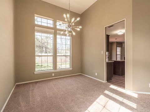A room with a carpeted floor, a chandelier, and a view of trees through the windows.