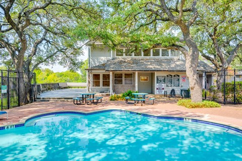 A pool in front of a house with a tree in front of the house.