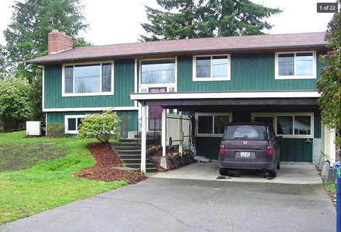 A green house with a car parked in front.