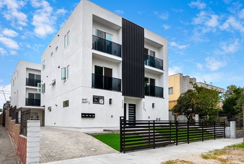 the exterior of a white apartment building with a black fence