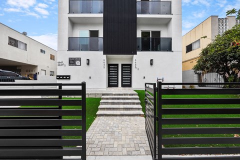 the front of a white house with a black fence and grass