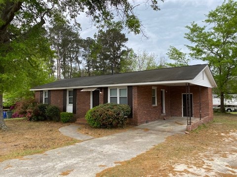 A small brick house with a white roof and a driveway in front.