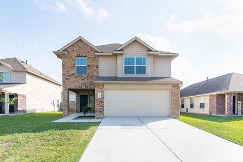a tan and brick house with a white sidewalk in front of it