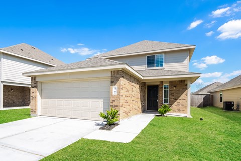 a tan brick house with a garage door and a lawn