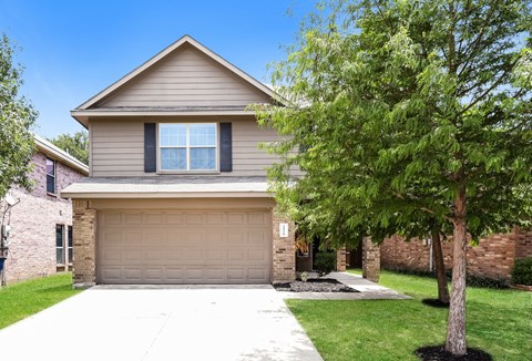 a tan house with a garage door and a tree