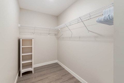 A white closet with a shelf and clothes hanging on a rack.