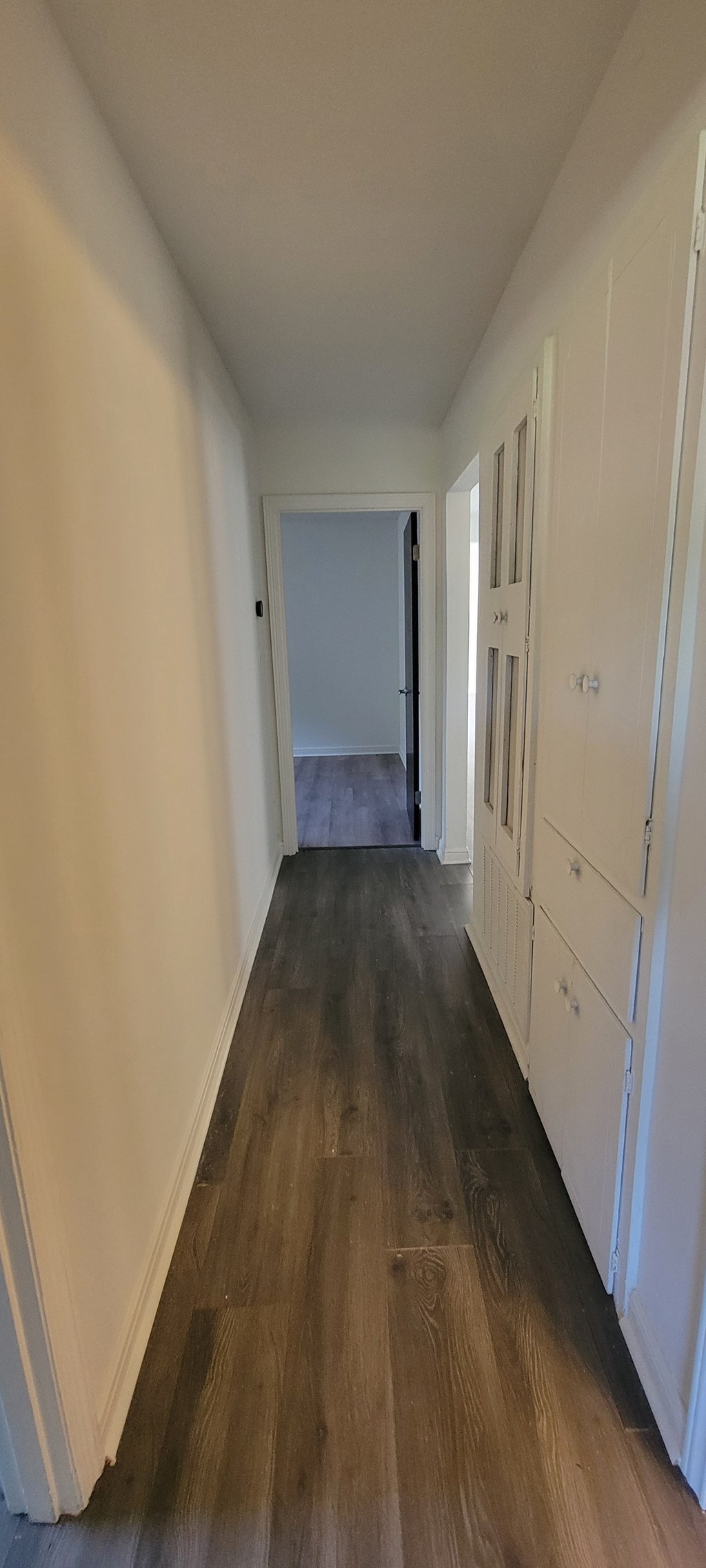 A long hallway with white walls and wood flooring.