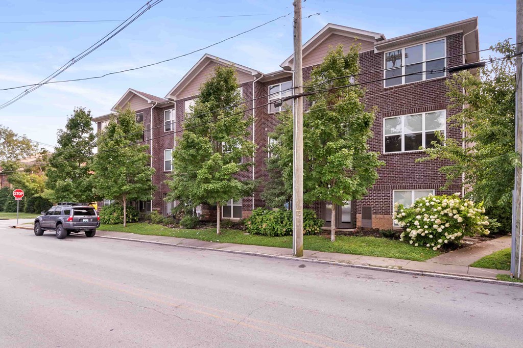 A street view of a residential area with a building on the right and a car on the road.