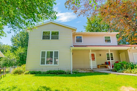 A house with a white door and windows is surrounded by greenery.