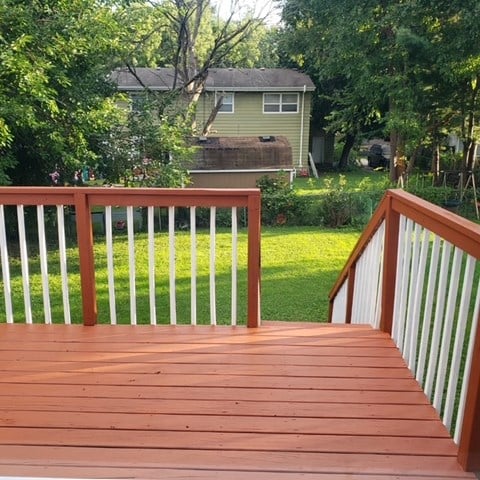 A wooden deck with a white railing and a green lawn.