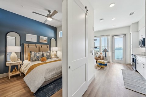 A bedroom with a bed and a ceiling fan, and a kitchen with a refrigerator and a sink.