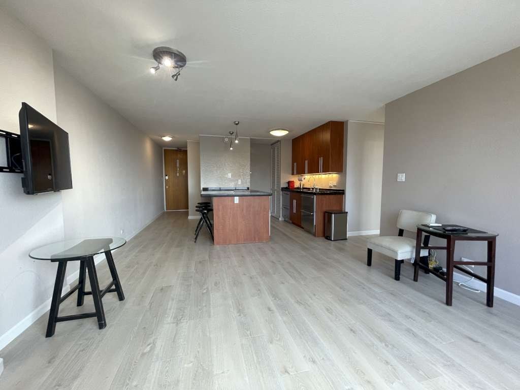 A living room with a television, a dining table, and a kitchenette.