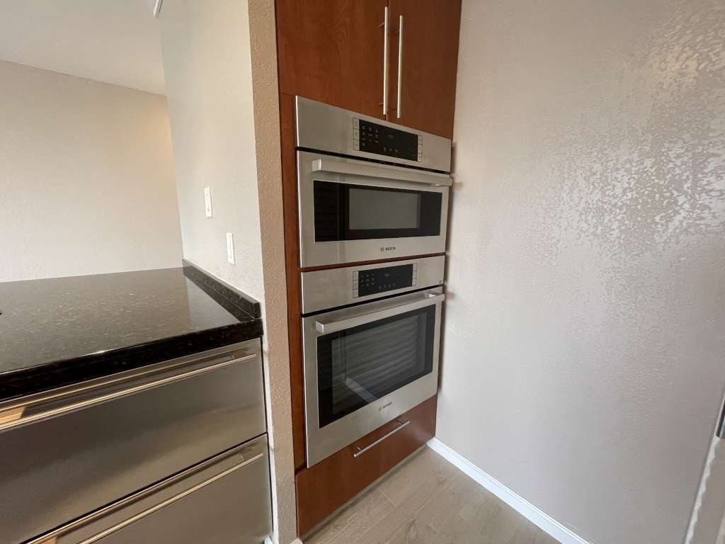 A kitchen with a stainless steel refrigerator and a wooden cabinet with three ovens.