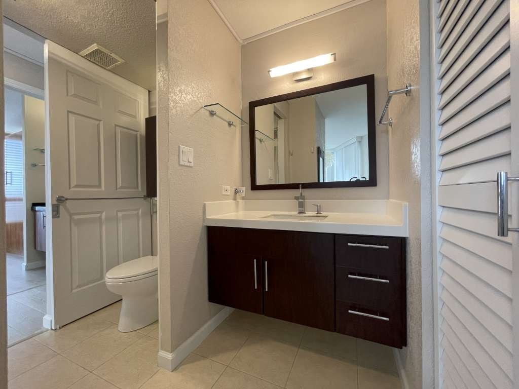 A bathroom with a white toilet, a sink with a mirror and brown cabinets.