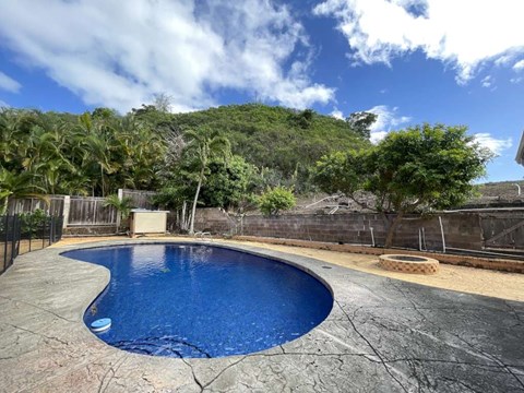 A blue swimming pool surrounded by a concrete patio and a fence.