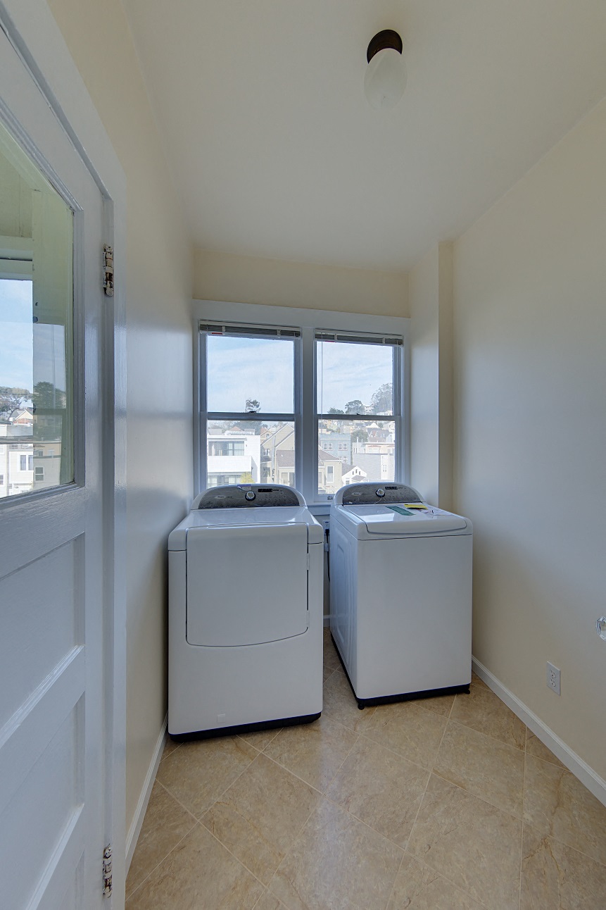 two washer and dryers in the corner of a room with windows
