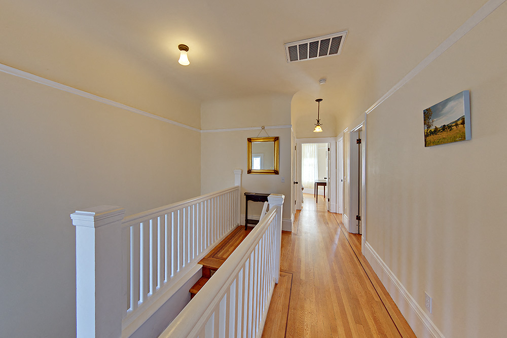 a long hallway with white railings and wood floors