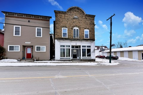 A building with a red door is situated in front of a building with a white door.