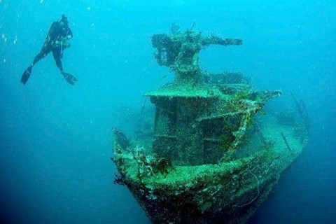 A diver swims next to a large, rusted shipwreck.