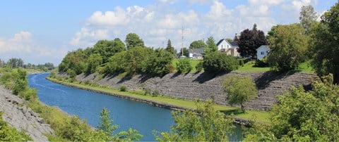 A river flows through a green landscape with a white house in the background.