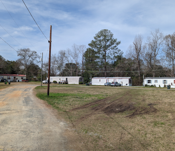 A rural landscape with a dirt road, utility pole, and white buildings.