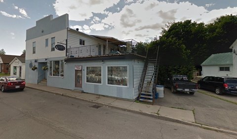 A white building with a balcony and a sign that says "Cafe" is surrounded by trees and parked cars.