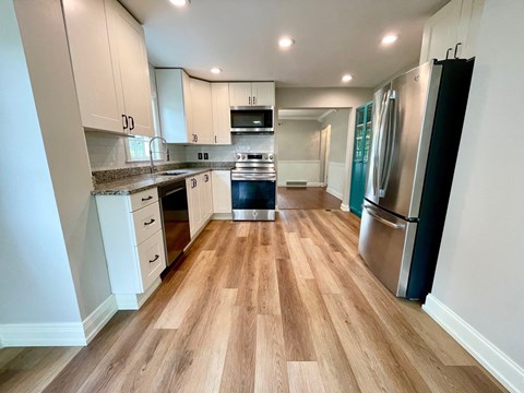 a kitchen with wood floors and white cabinets and stainless steel appliances