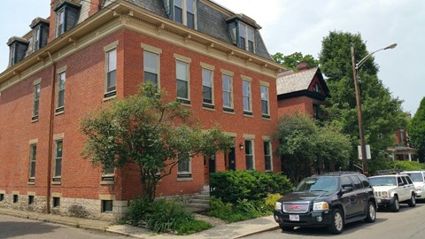 A black car is parked on the side of a street in front of a red brick building.