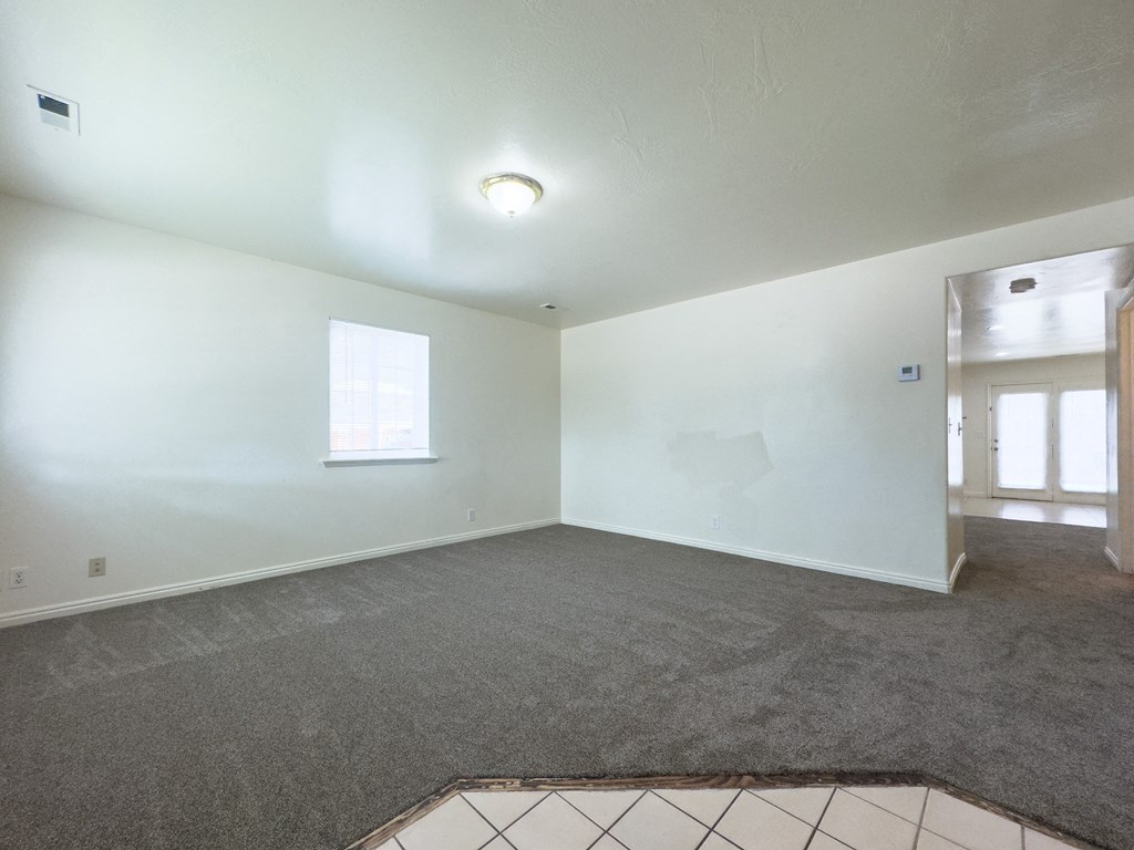 A room with a grey carpet and a window.