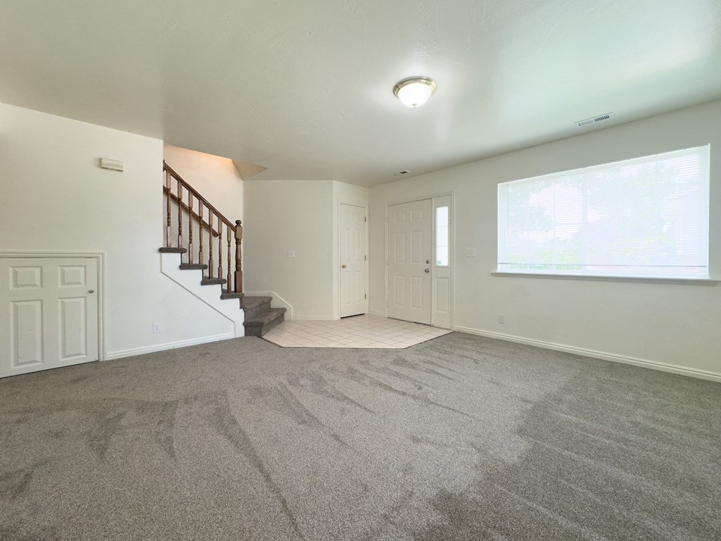 A spacious room with a carpeted floor and a staircase with a wooden railing.