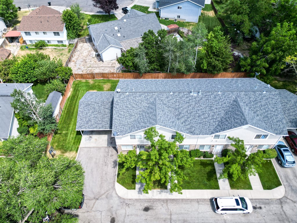 A large house with a grey roof is surrounded by trees and a driveway.