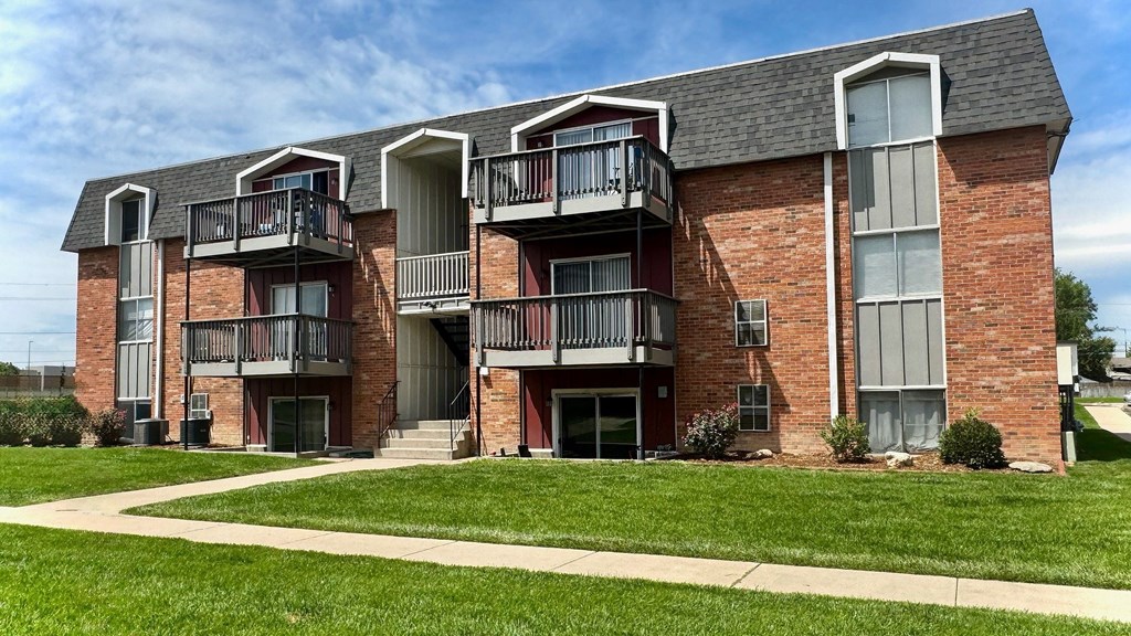 A red brick apartment building with balconies and a green lawn in front.