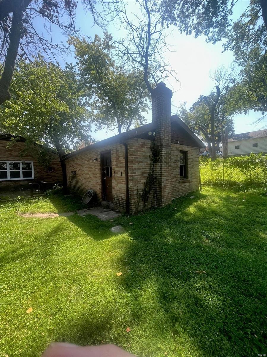 a small brick house in a yard with grass and trees
