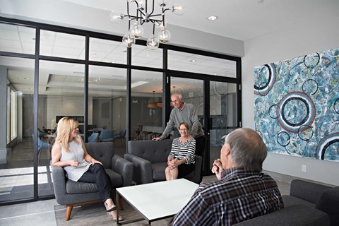 A group of people are sitting in a room with a large painting on the wall.