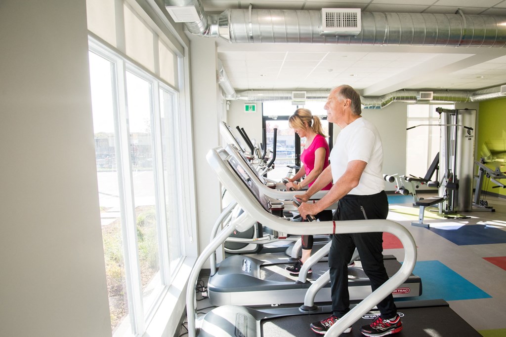 two people walking on a treadmill in a gym