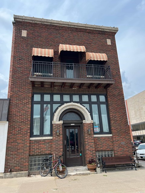 A red brick building with a black door and a balcony with orange awnings.