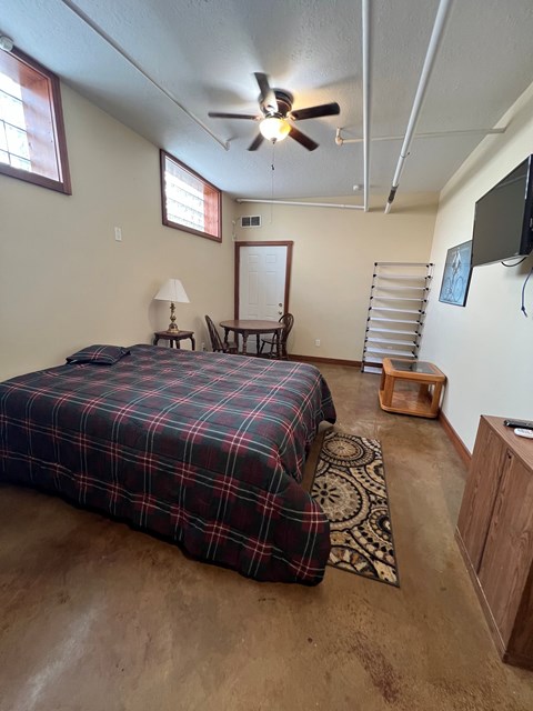 A bedroom with a bed, a chair, a table, and a ceiling fan.