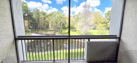 A balcony with a black railing and a window overlooking a green lawn and trees.
