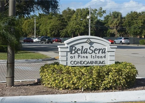 A sign for BelaSera at Pine Island Condominiums is in front of a parking lot.