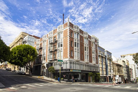 A street view of a large, multi-story building with a red brick facade and white trim.